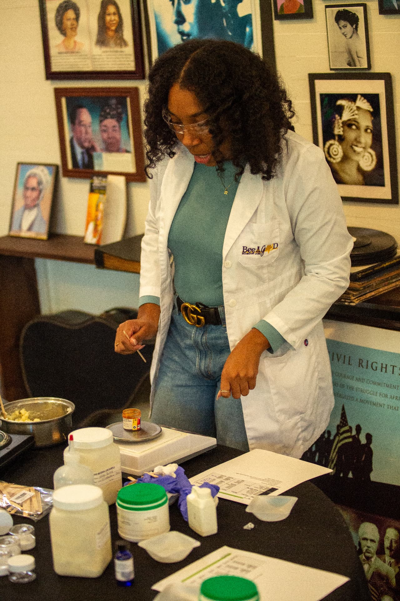A scientist in a lab coat weighs ingredients on a scale during a STEM Day cosmetics lab activity.