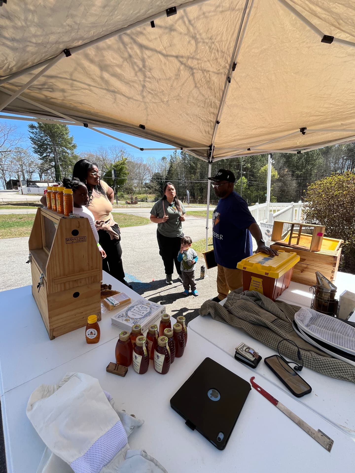 A beekeeper in a NAACP T-shirt shows beekeeping suits, tools and honey jars to a family under the STEM Day tent outside the museum.
