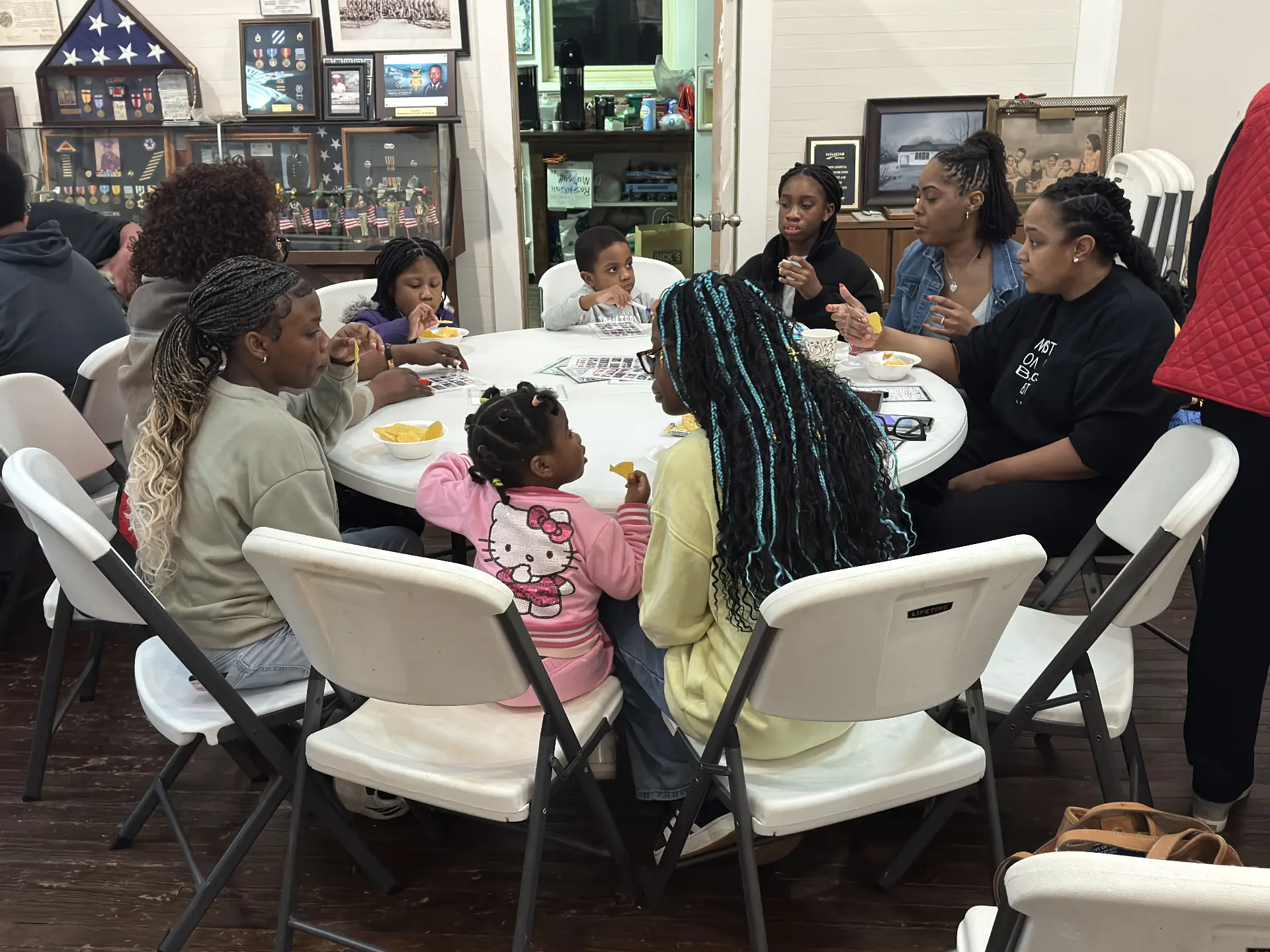 Families with children share snacks and play bingo together at a round table during game night.