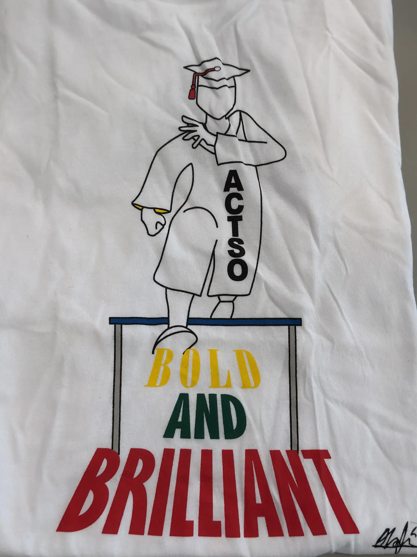 A white ACT-SO t-shirt reading "Bold and Brilliant" with a graduate figure printed on the front.
