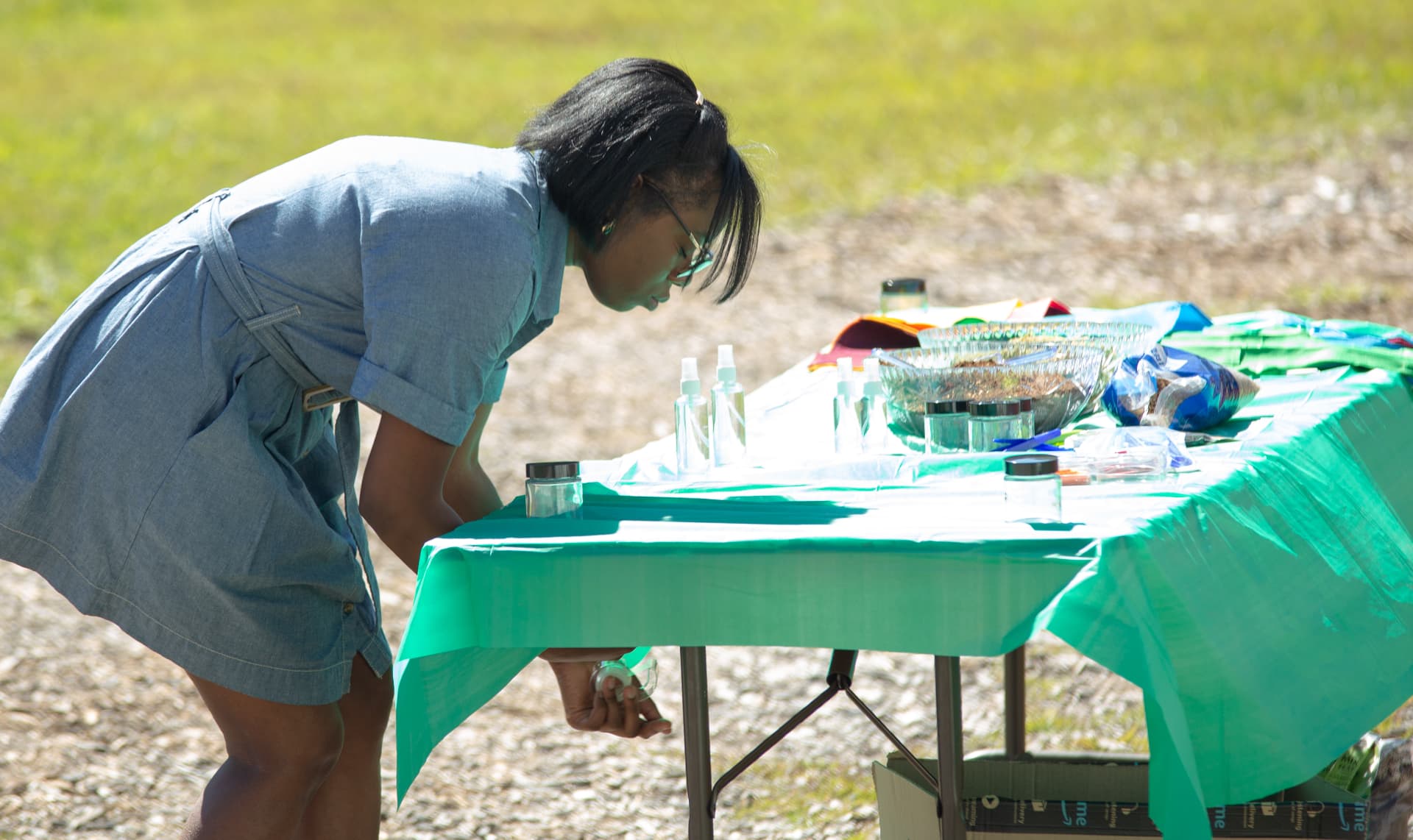 A volunteer sets out jars, spray bottles and soil bowls on an activity table before a STEM Day session.