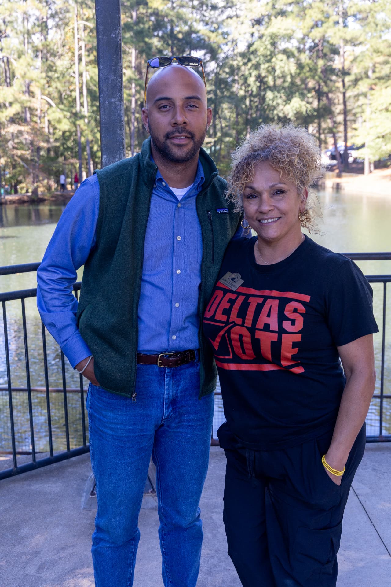 A couple poses together by the lake, the woman wearing a black Deltas Vote t-shirt.