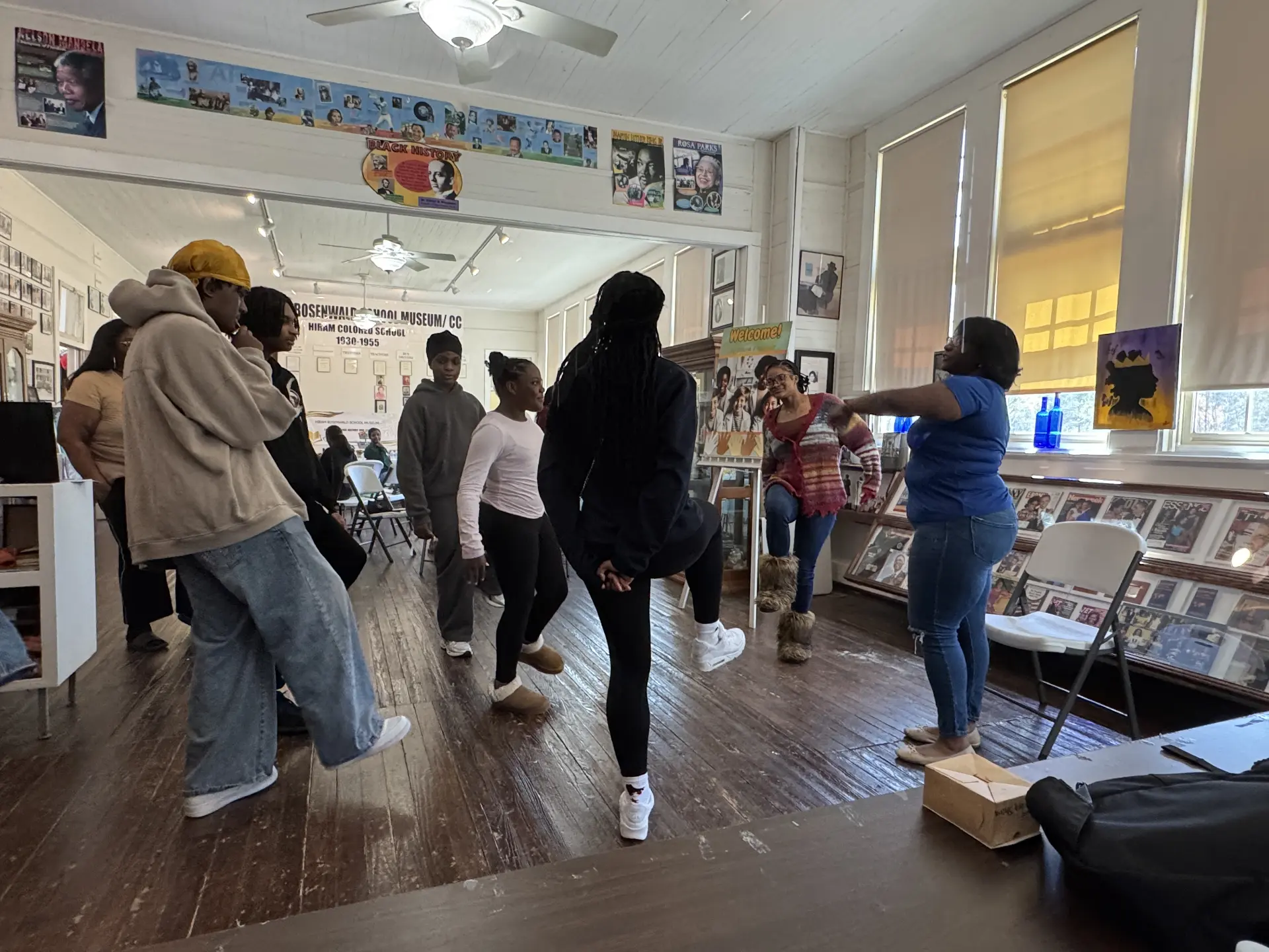 Students and instructors step and move together in a movement activity on the museum's wood floor.