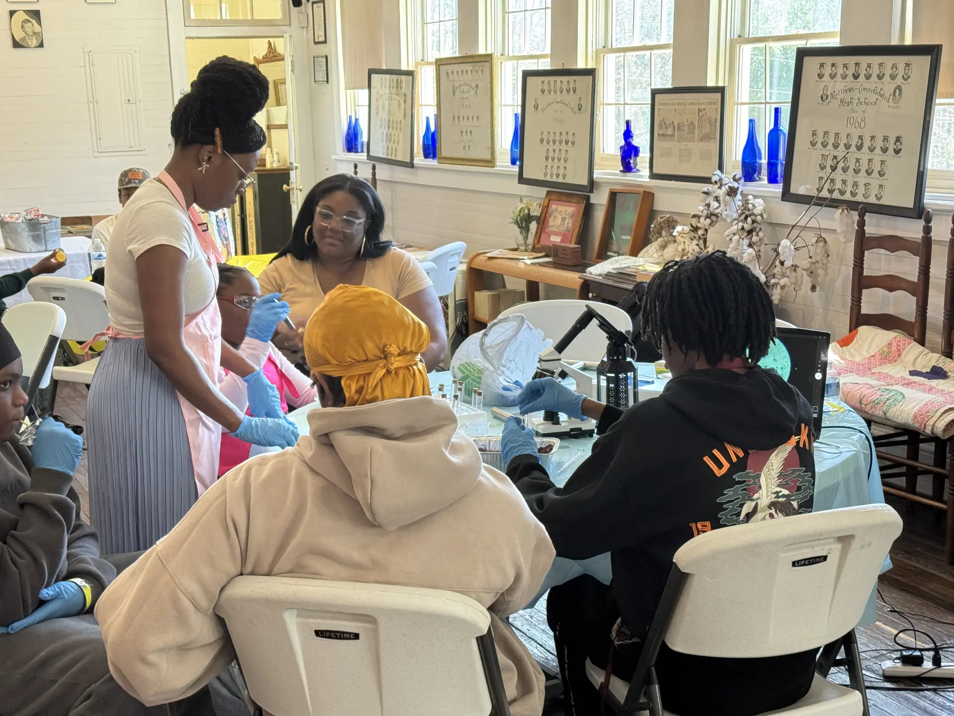 Students in gloves use a microscope and test tubes with an instructor among the museum's class photos.