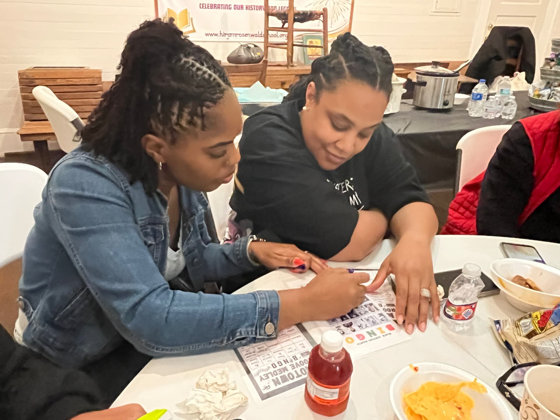 Two guests lean in to mark a Motown Groove Medley bingo card together during game night.