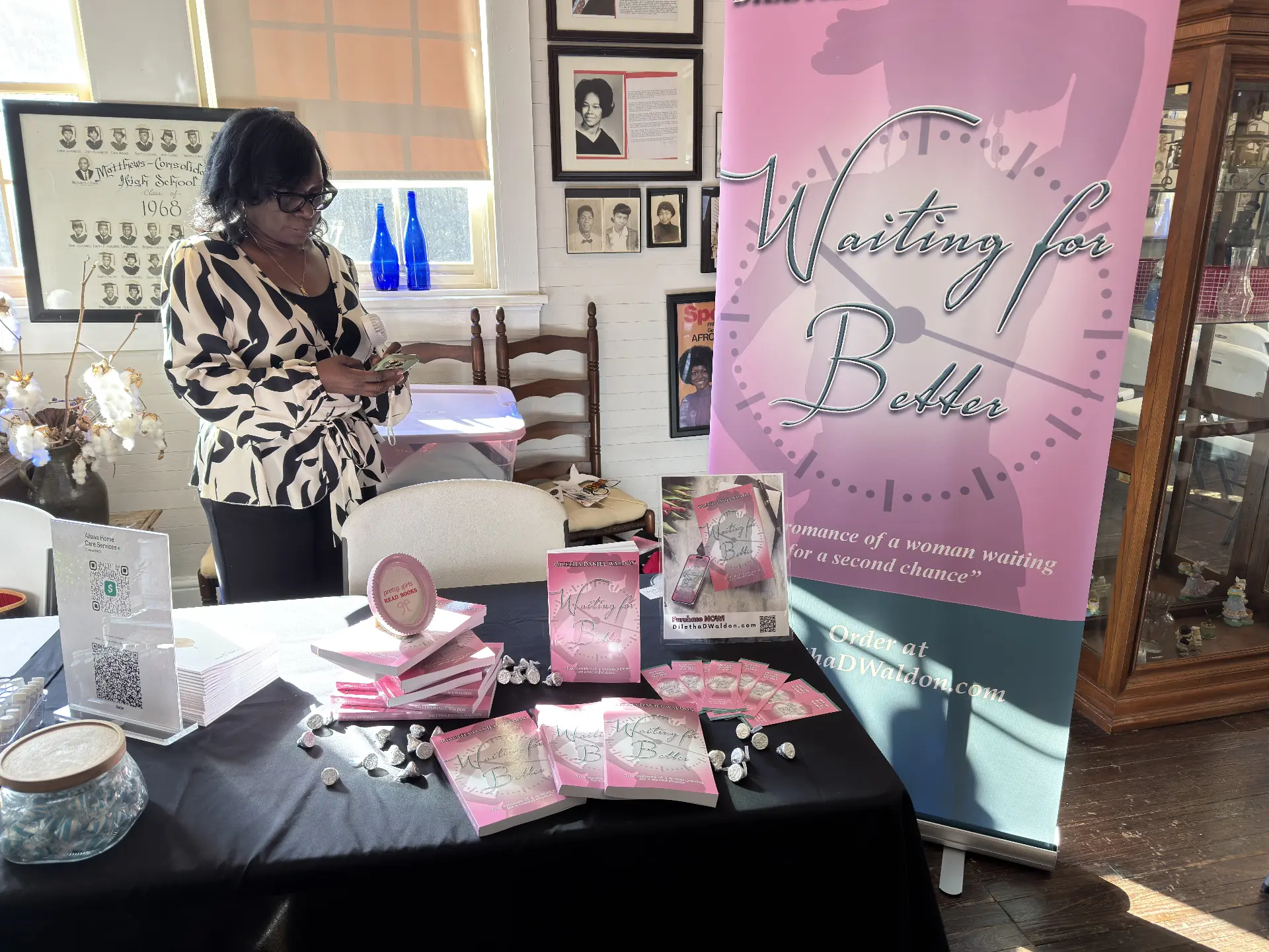 An author stands at her table of Waiting for Better books in front of a pink promotional banner inside the museum.