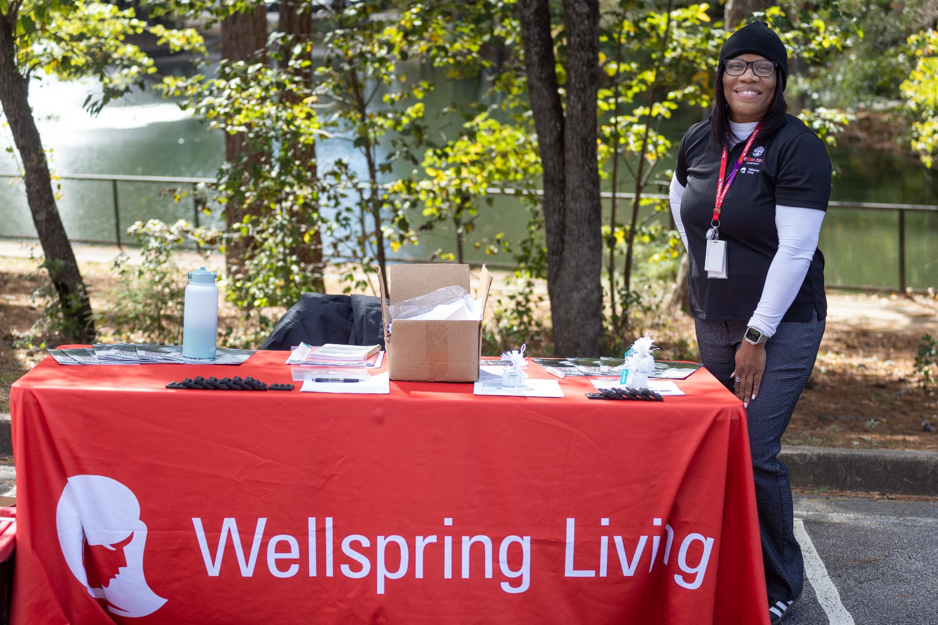 A smiling vendor stands behind the Wellspring Living information table at the block party.