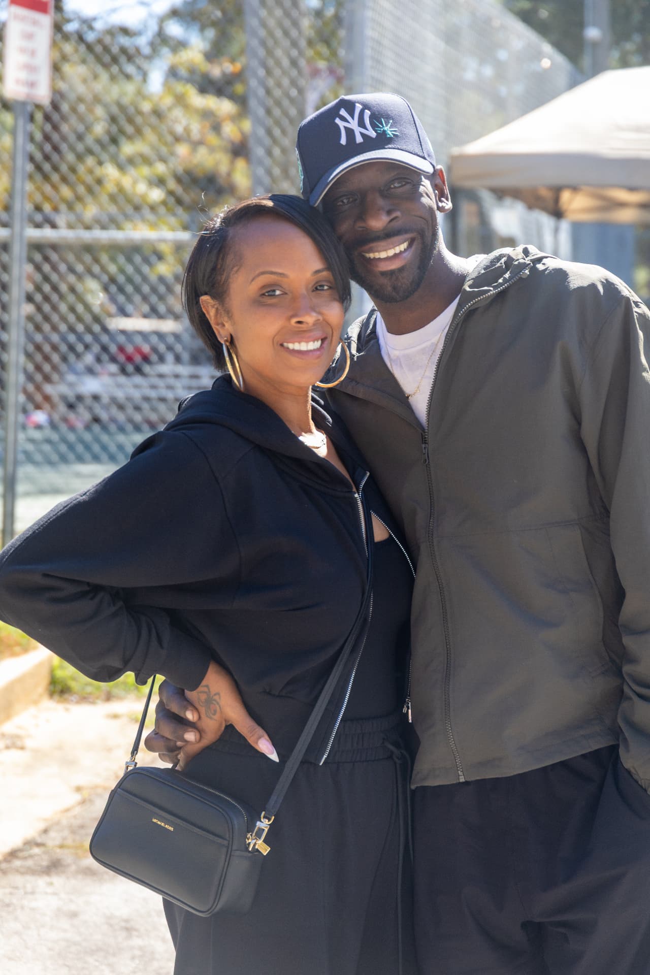 A smiling couple poses together near the fence at the block party.