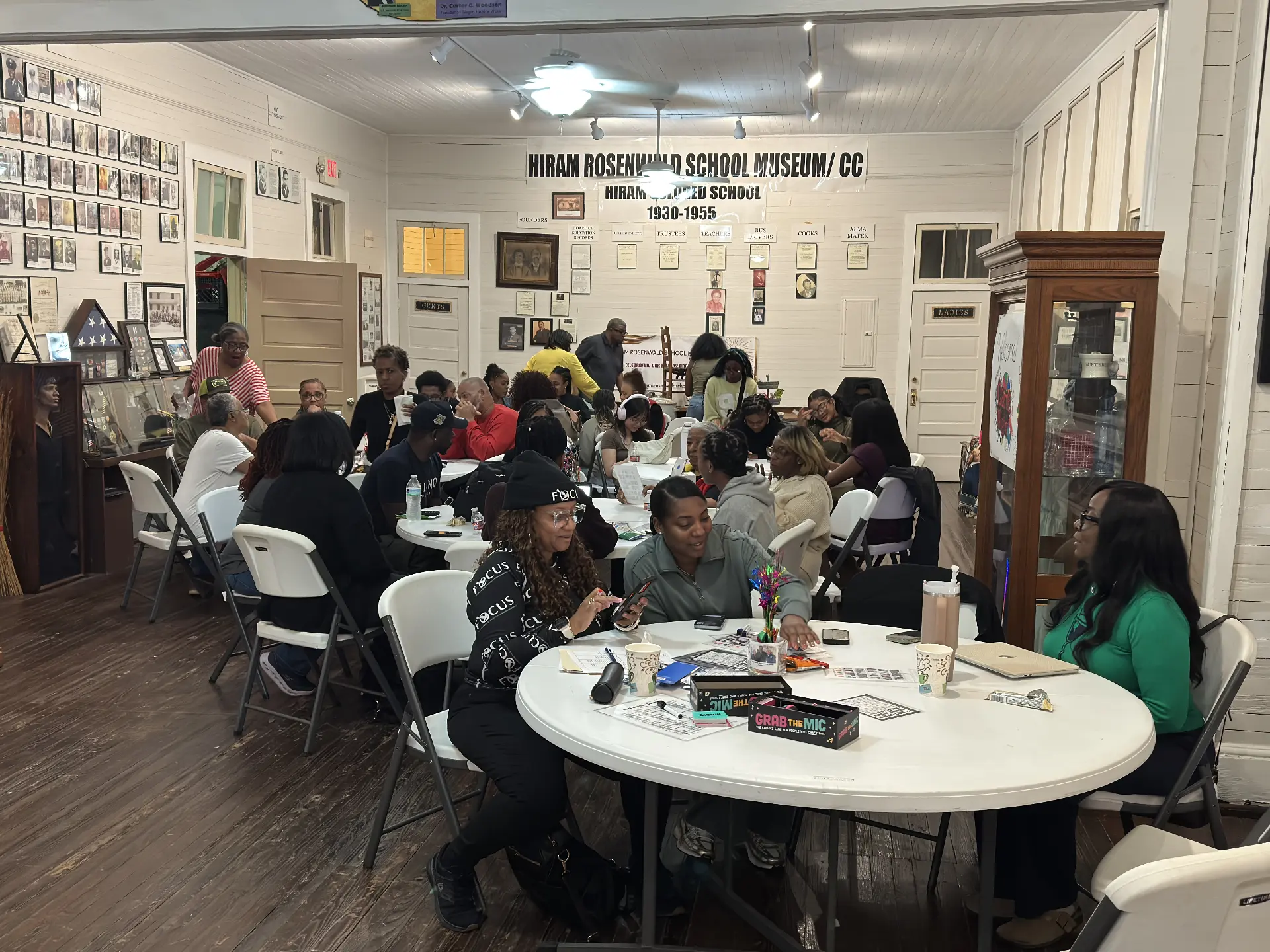 A crowd of guests gathers at tables playing games beneath the Hiram Rosenwald School Museum banner.