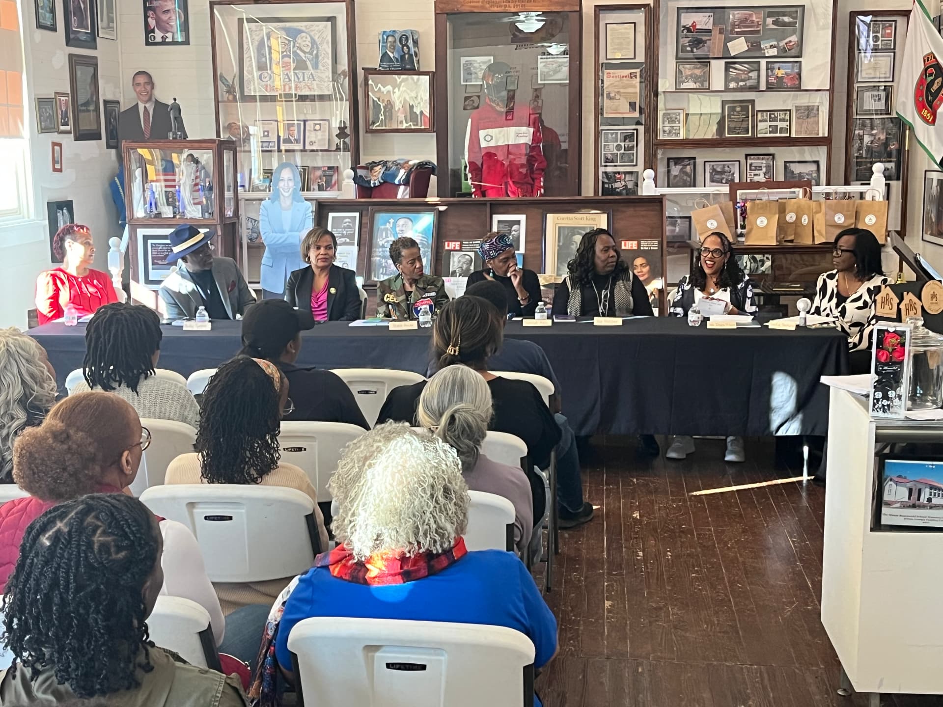 A panel of authors and speakers seated at a long table talks with an audience seated in the museum.