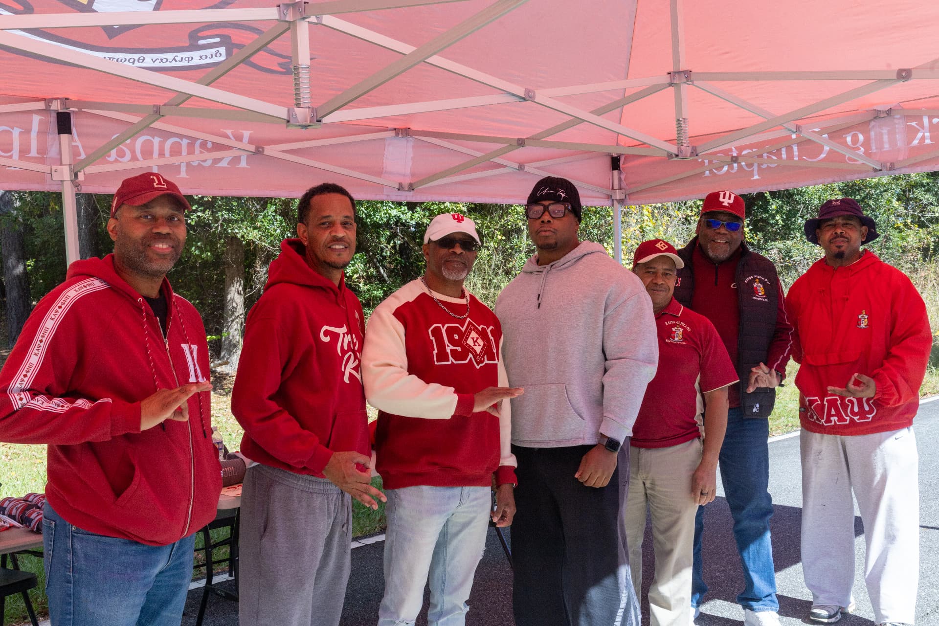 Members of Kappa Alpha Psi Fraternity pose together in red and white under their tent at the block party.