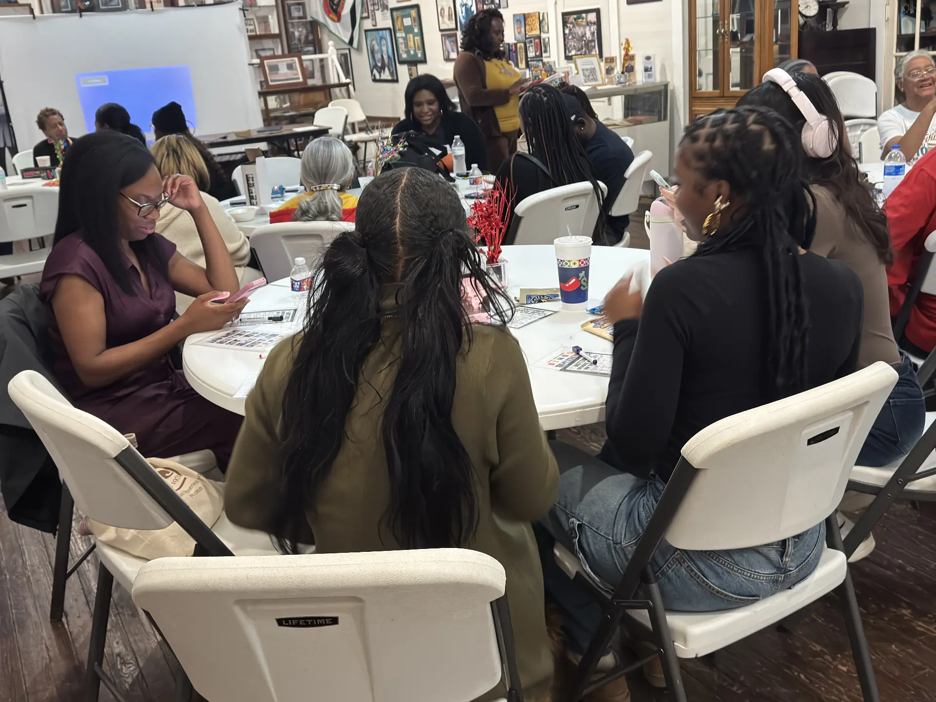 Guests study their bingo cards at a table while an organizer reads questions in the background.