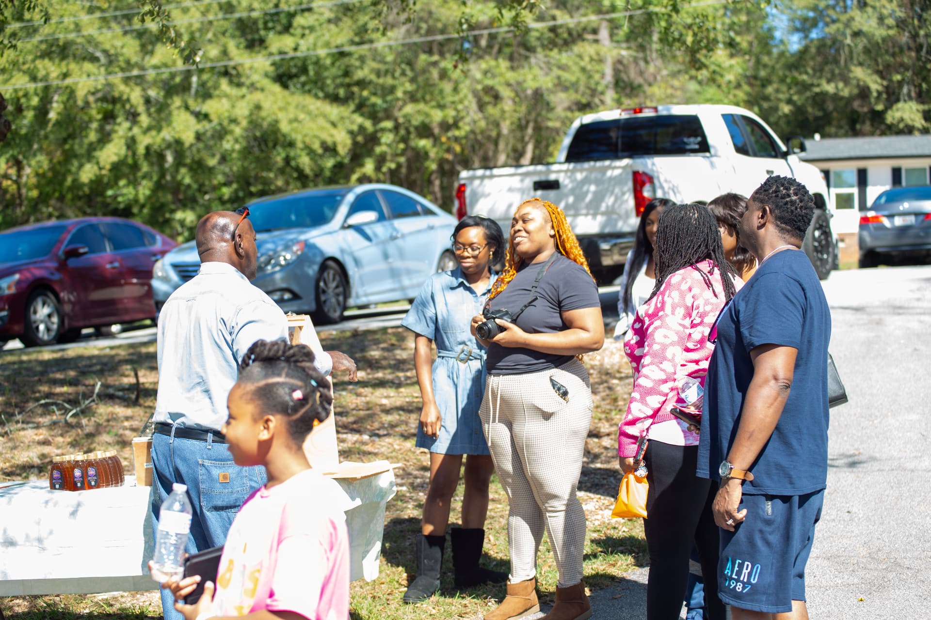 Visitors chat near a table of honey jars outside the schoolhouse during STEM Day.