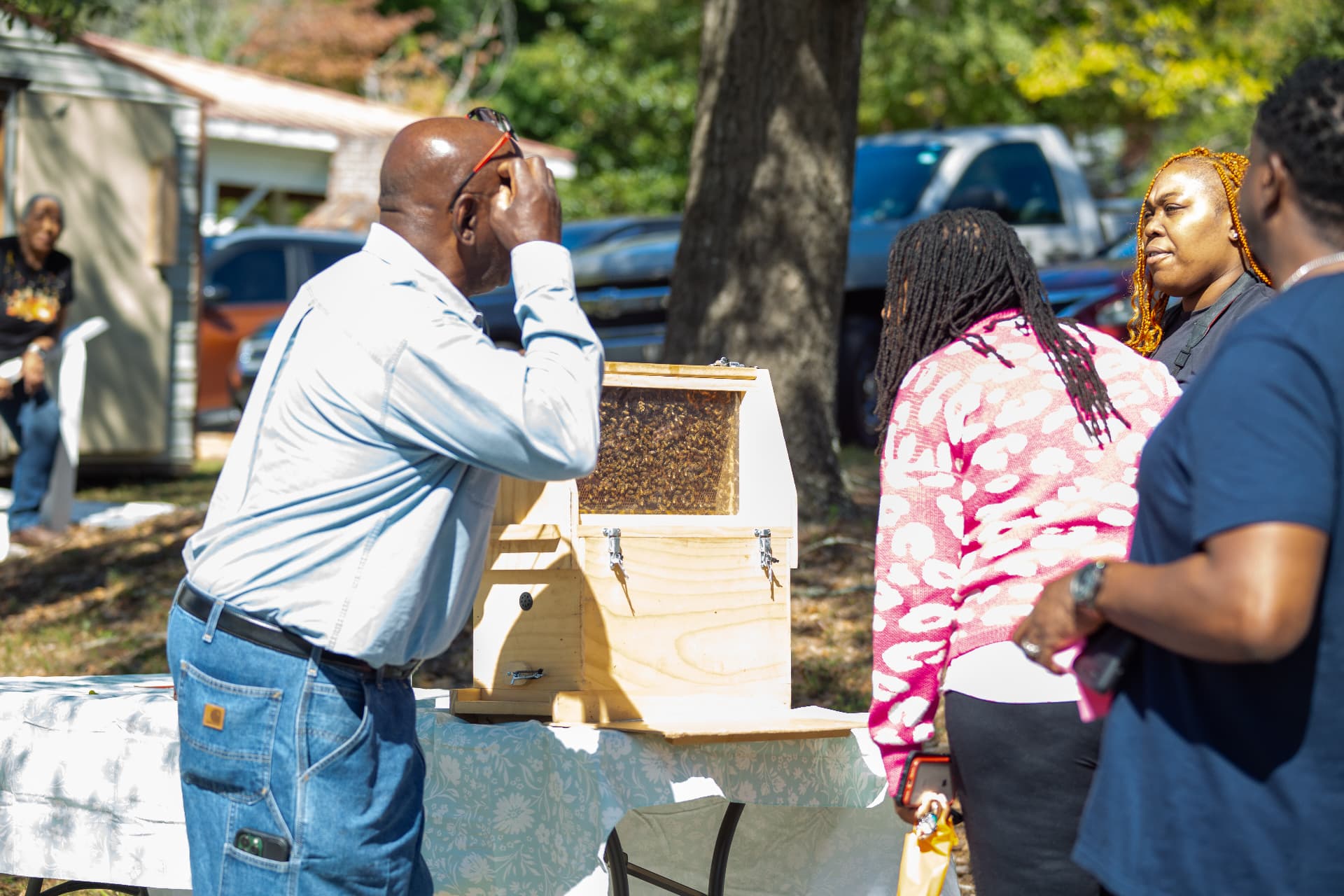 A beekeeper presents the glass-sided observation hive to a group of visitors outdoors during STEM Day.