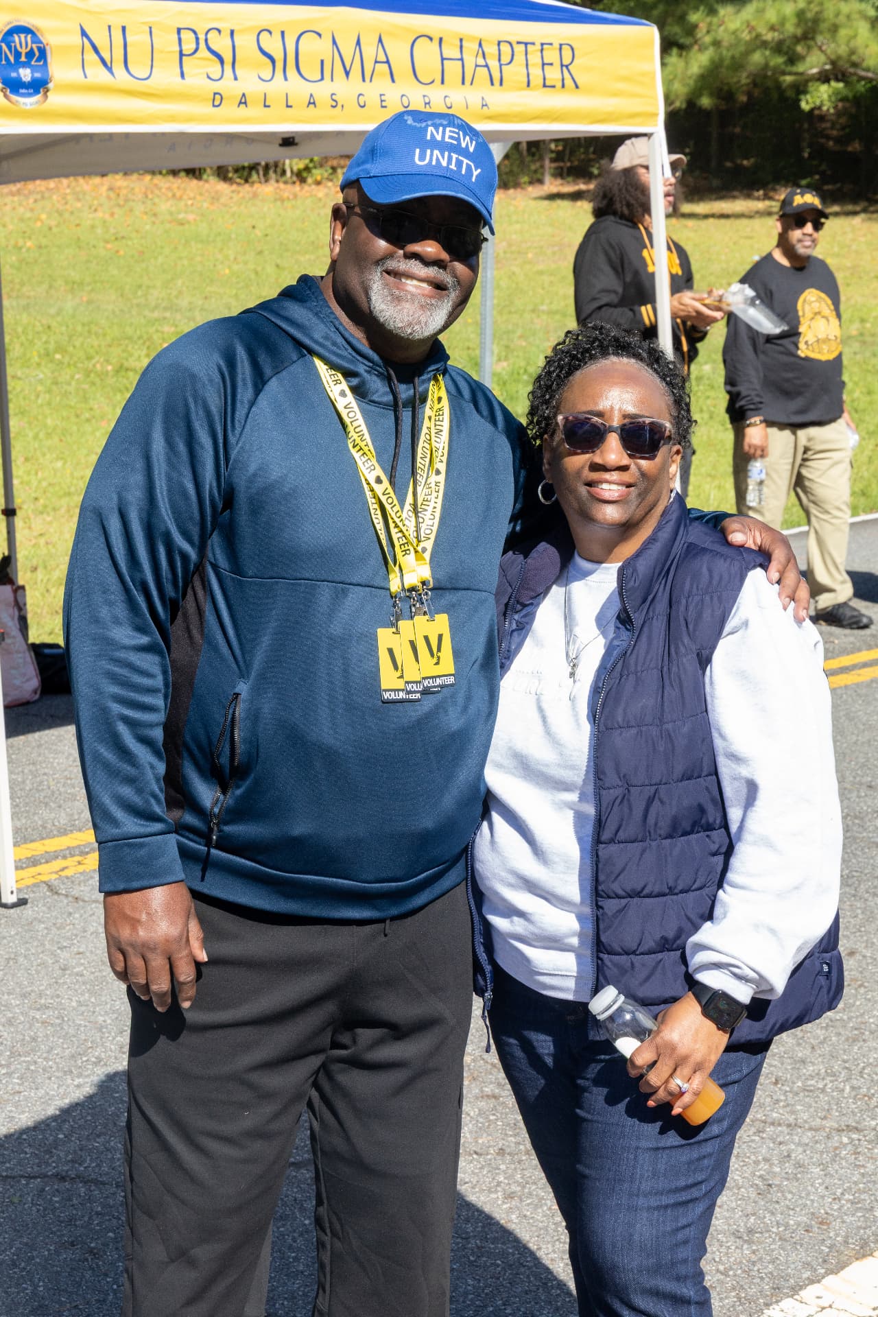 Two volunteers pose in front of the Nu Psi Sigma Chapter of Dallas, Georgia tent at the block party.