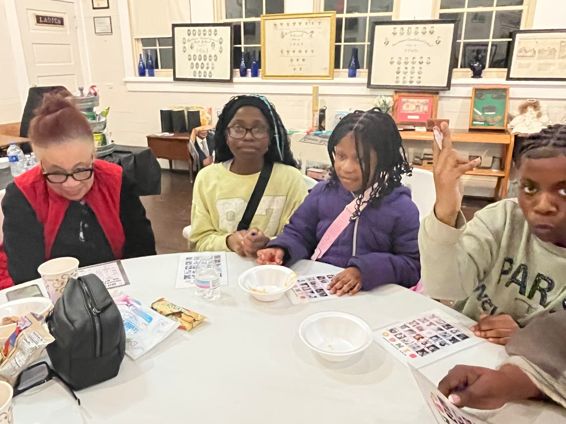 Guests around a table play Black History bingo in the museum's former classroom with vintage class photos on the windowsill.