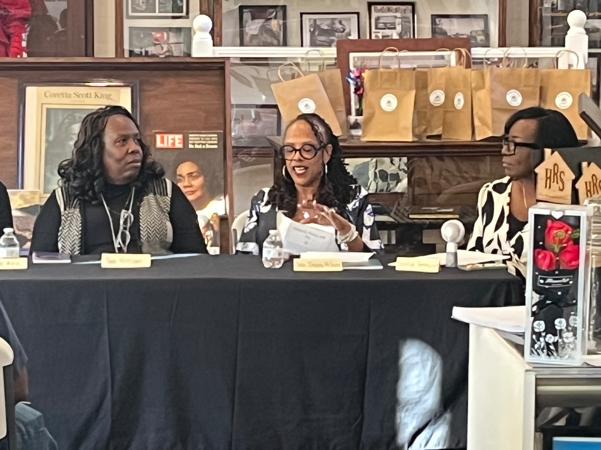A panelist shares remarks at the Authors Showcase table in front of gift bags and framed portraits.