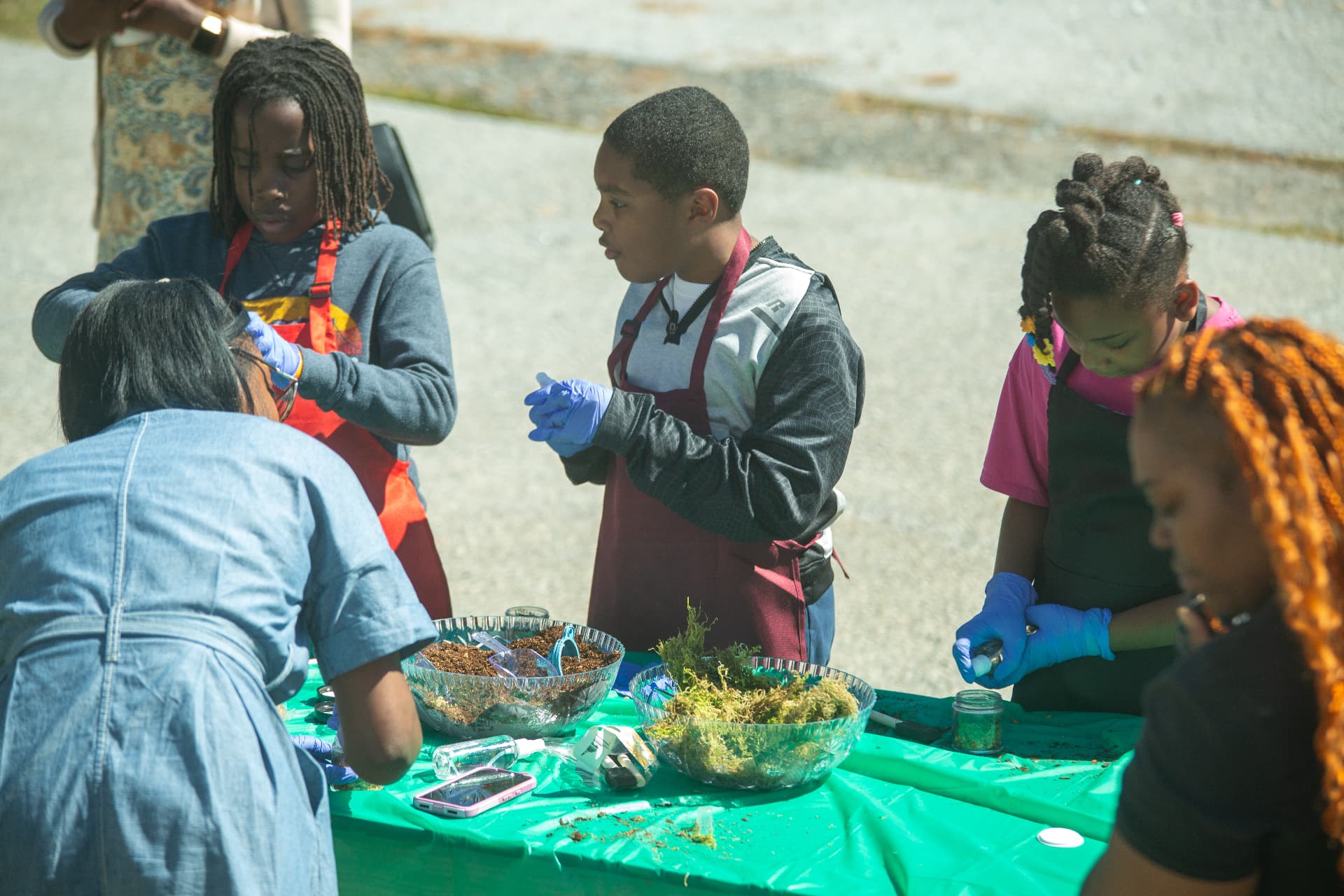 Students in aprons and gloves work together at the STEM Day terrarium-making table.