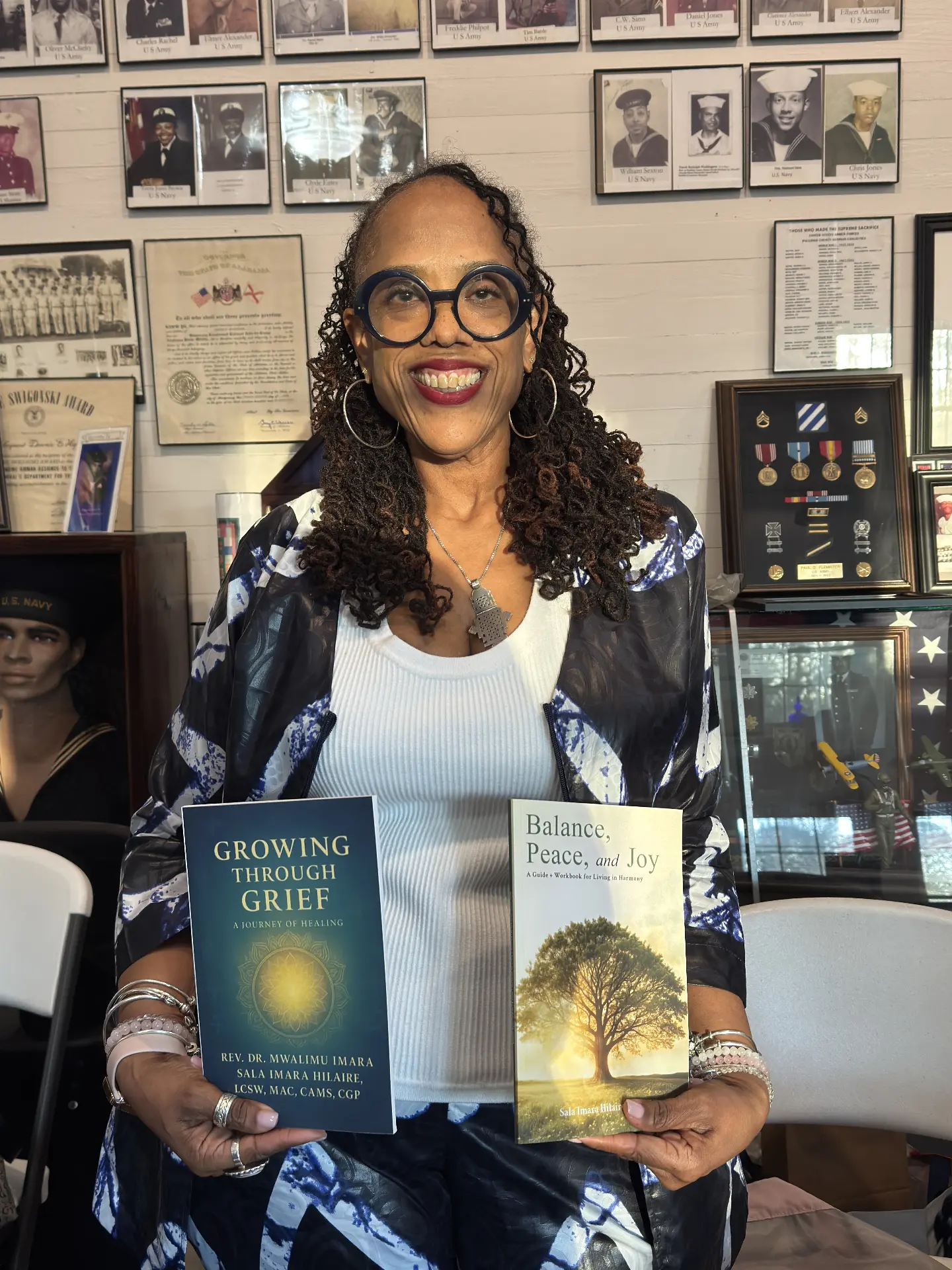 A smiling author holds copies of Growing Through Grief and Balance, Peace, and Joy in the museum.