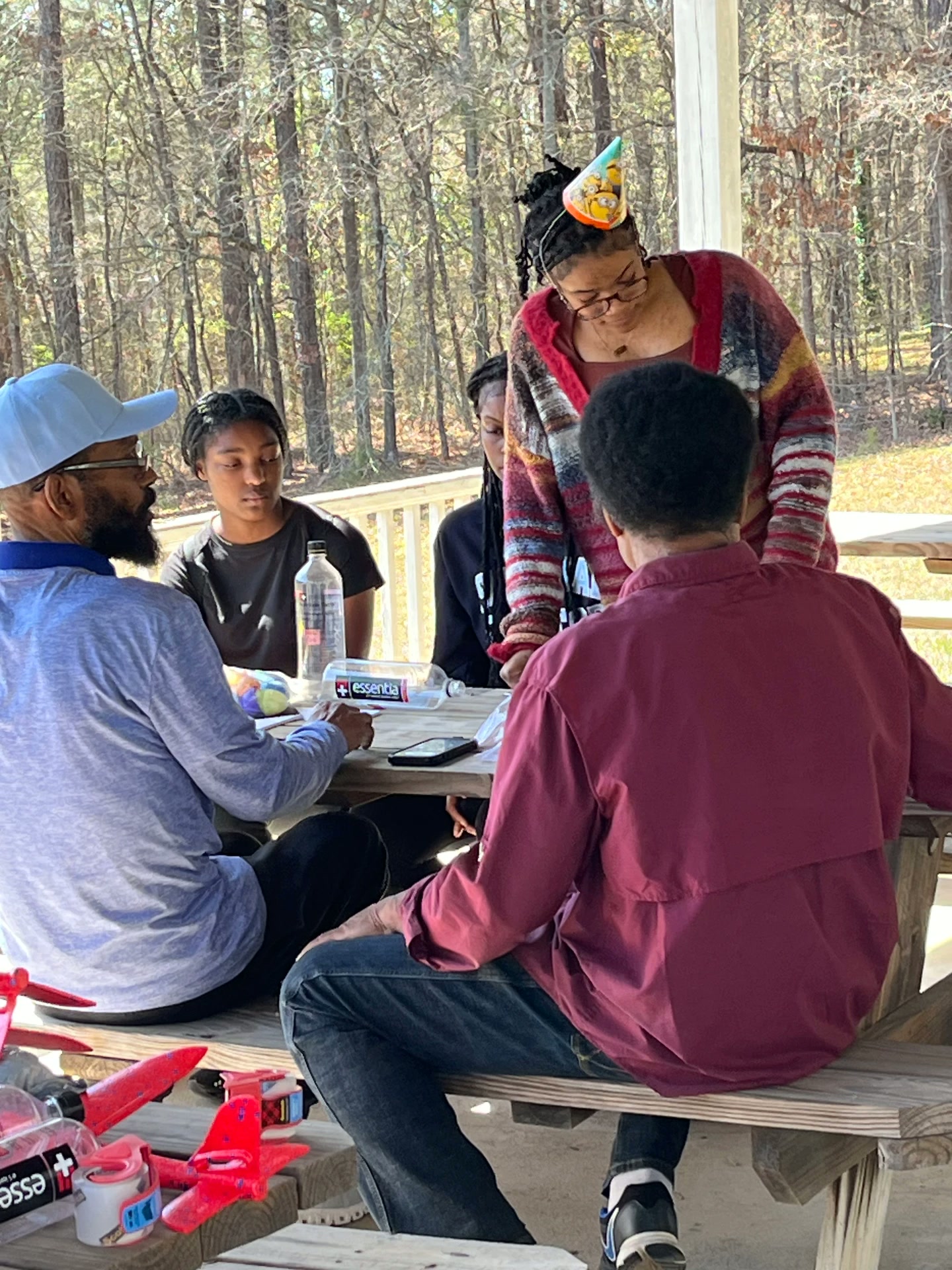 Adults and students gather around a picnic table under the pavilion working on a STEM Day craft project.