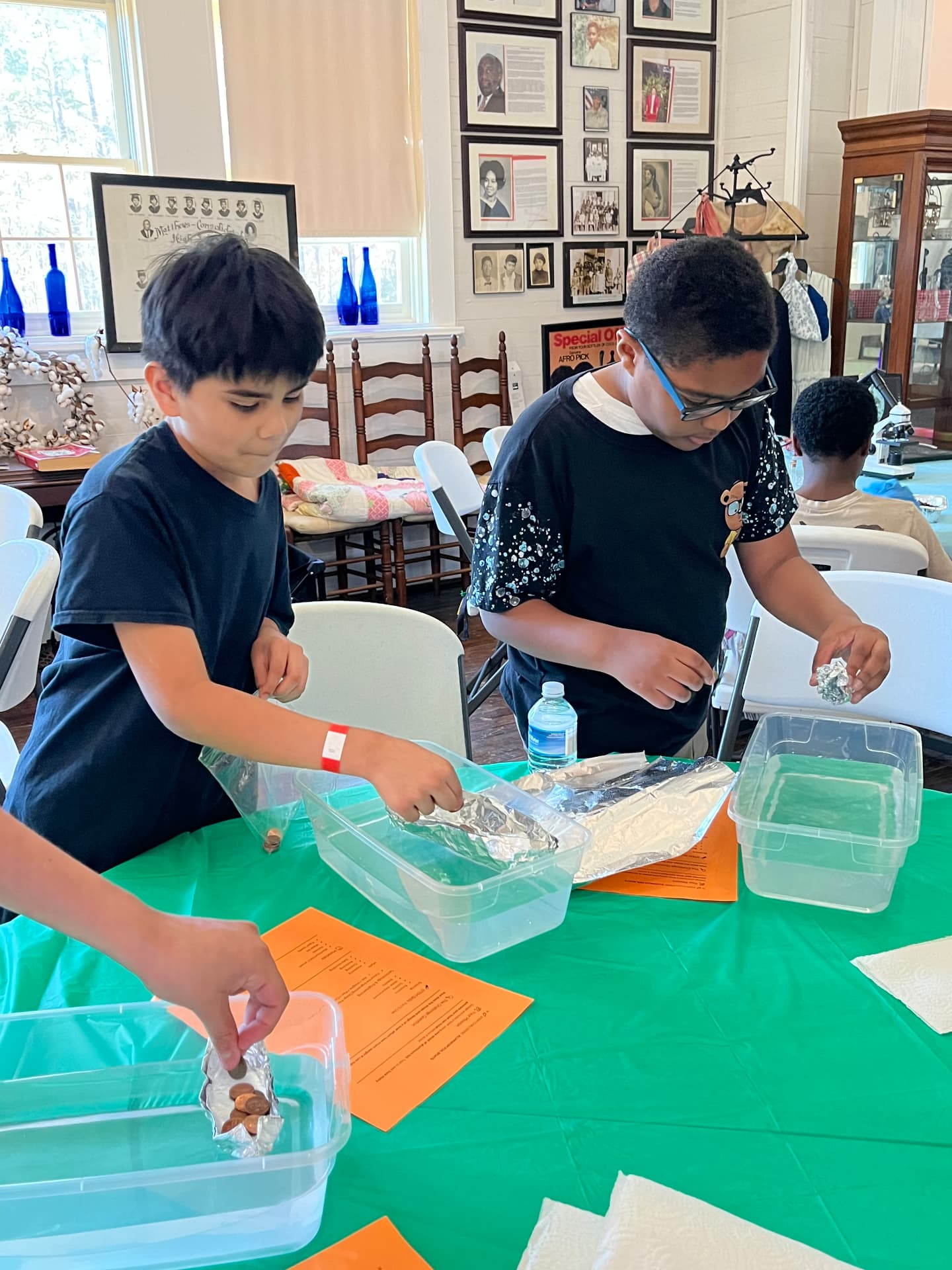 Two students load pennies into their foil boats floating in water bins during the STEM Day challenge.