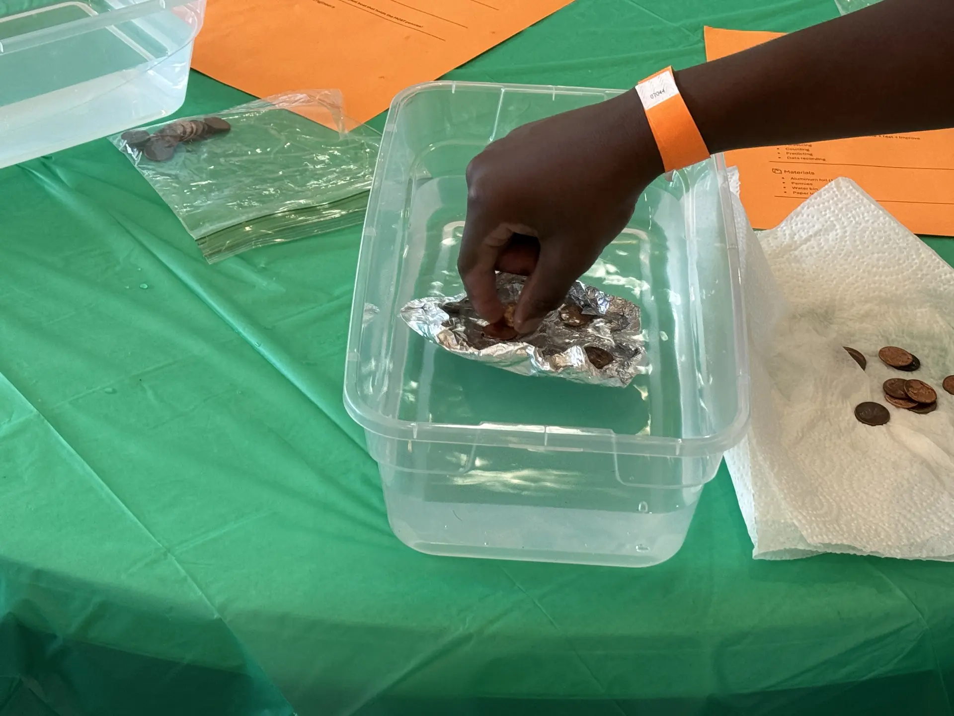 A child adds pennies to a foil boat floating in a water bin during the STEM Day boat-building challenge.