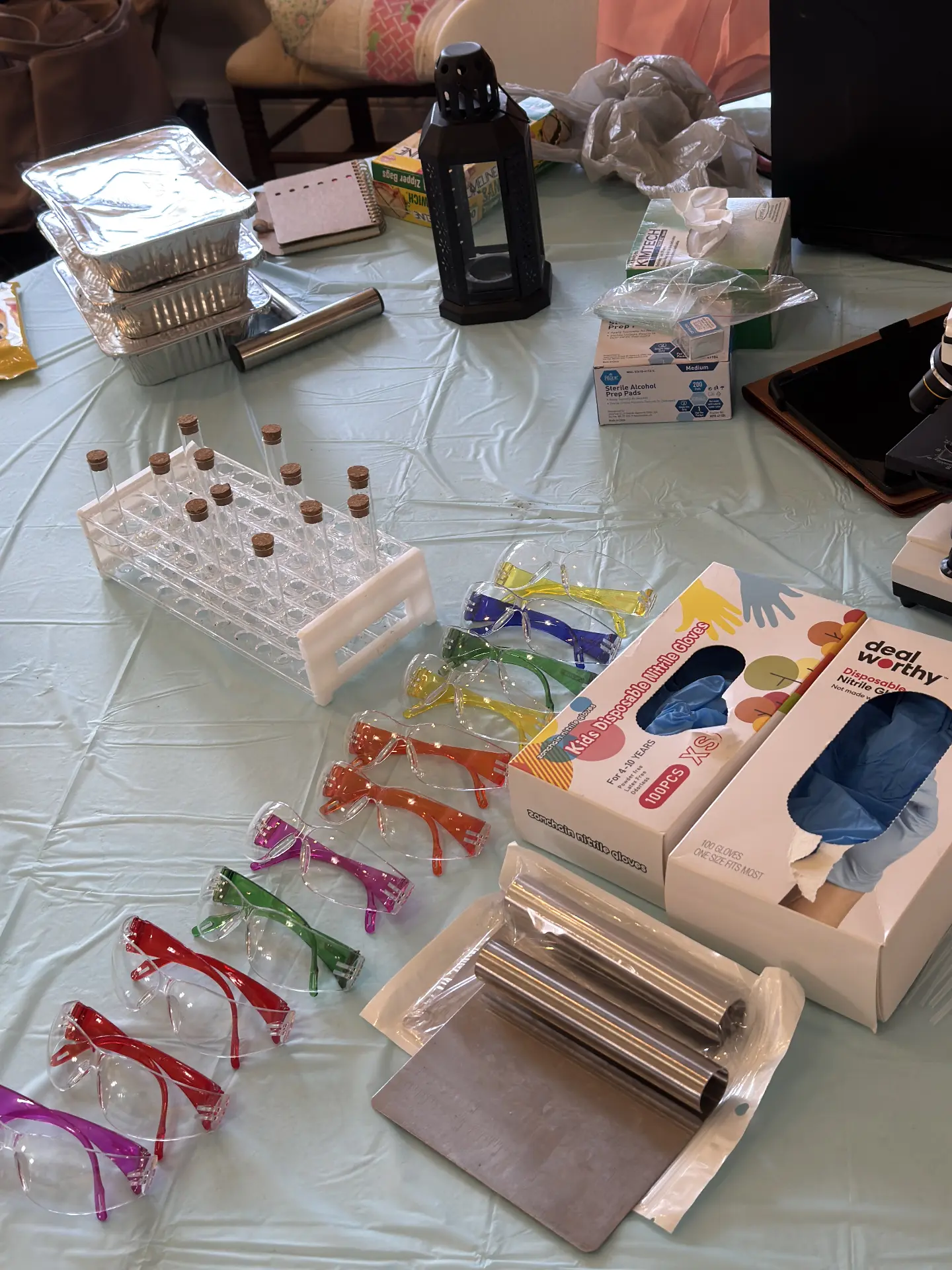 Lab supplies laid out for STEM Day activities: corked test tubes in a rack, colorful safety goggles, nitrile gloves and metal rolling pins.