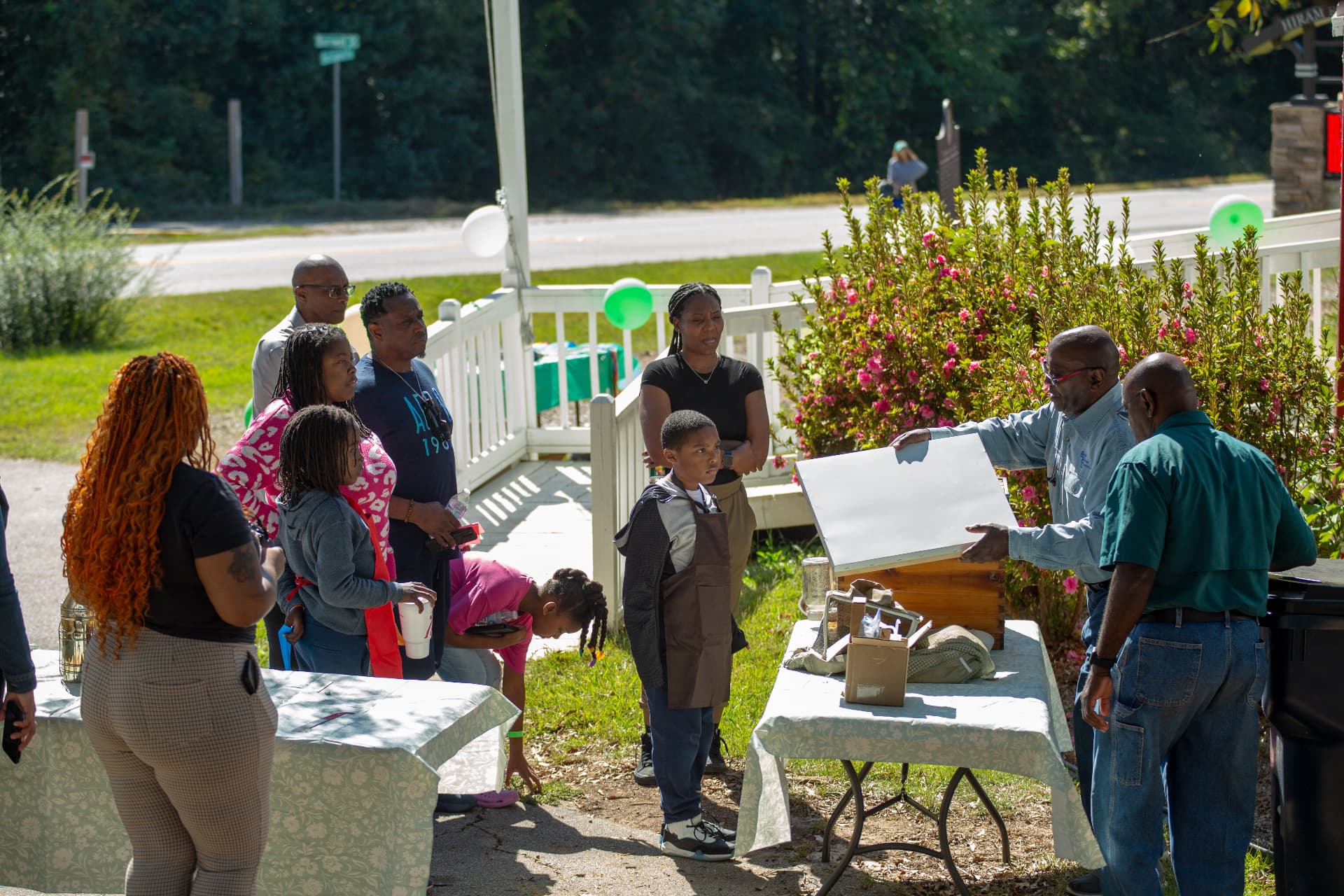 Two beekeepers open a wooden hive box for a group of families gathered outside the museum.