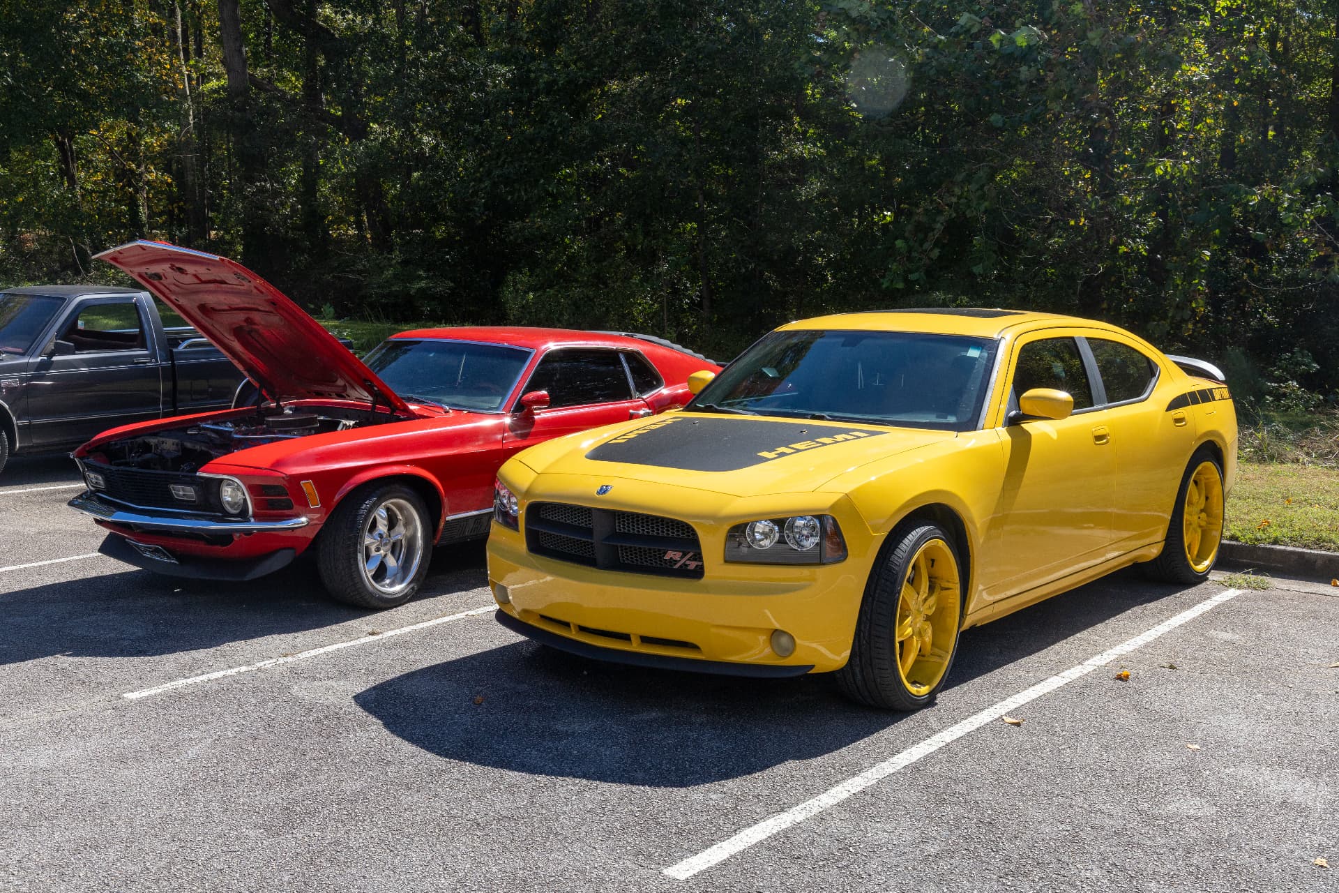 A yellow Dodge Charger R/T with a HEMI hood and a red classic Ford Mustang with its hood open at the block party car show.
