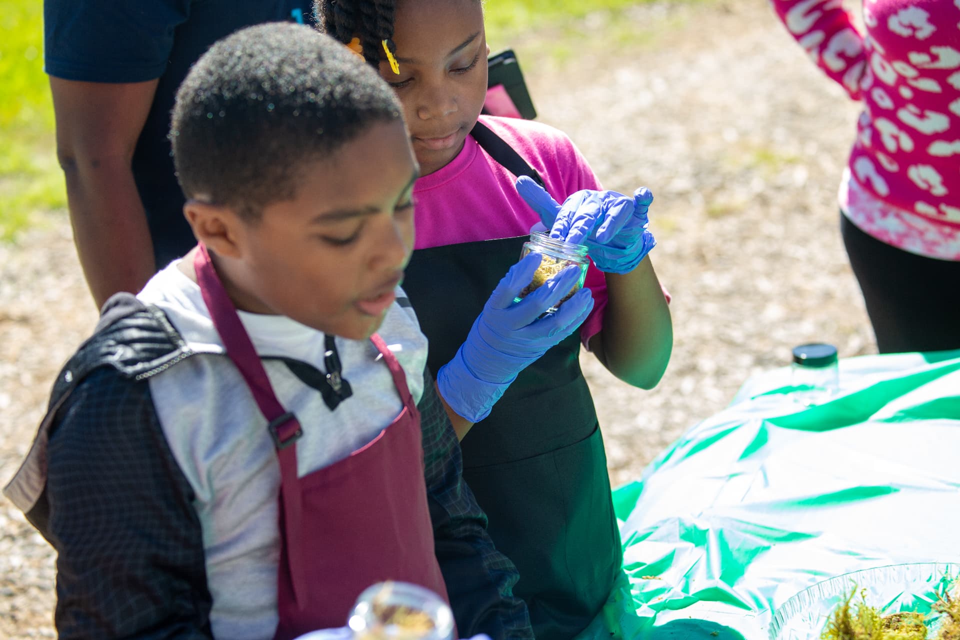 A student in gloves fills a small jar with soil and moss during the terrarium activity.
