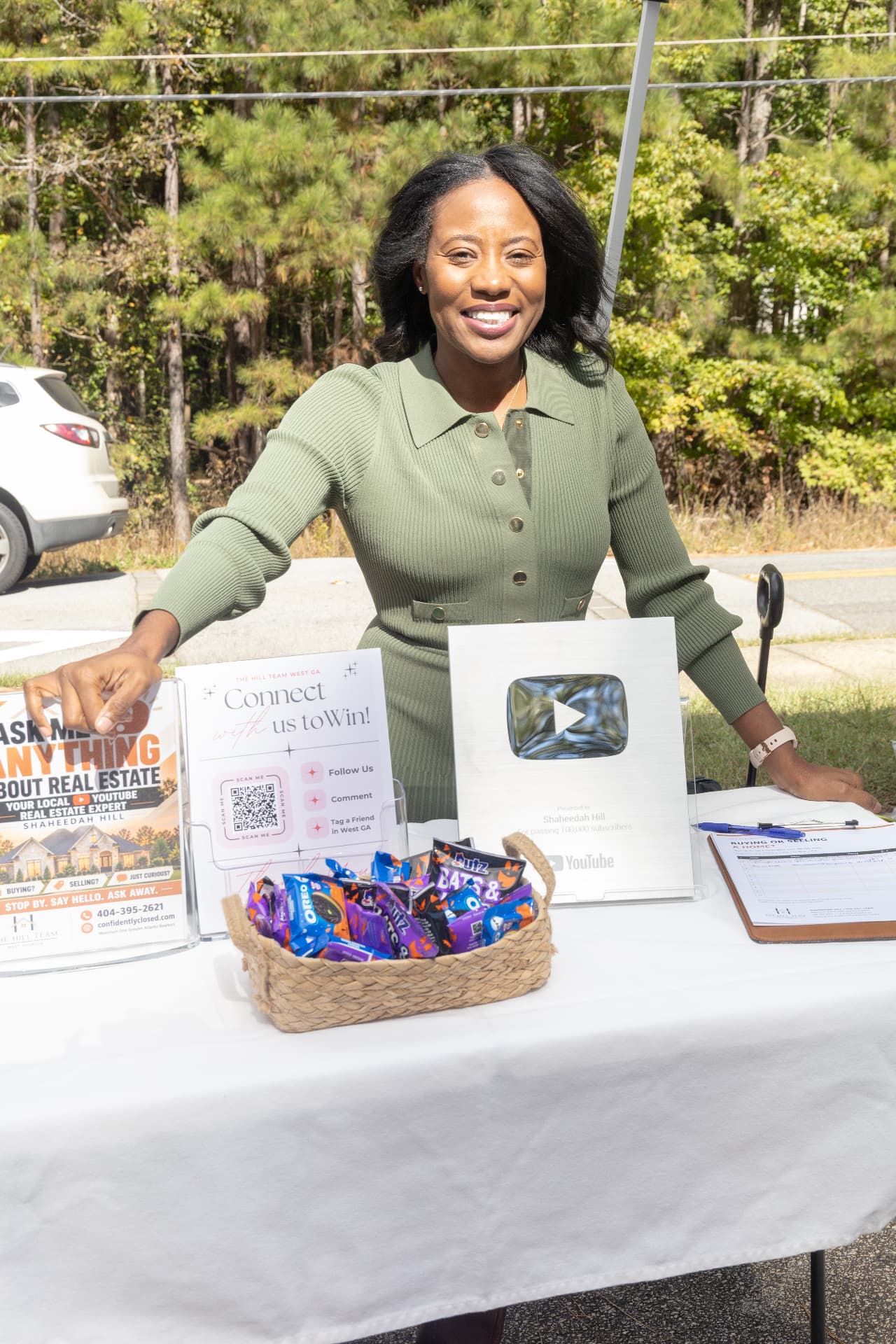 A real estate vendor smiles behind her table with a basket of Halloween candy and a YouTube creator award on display.