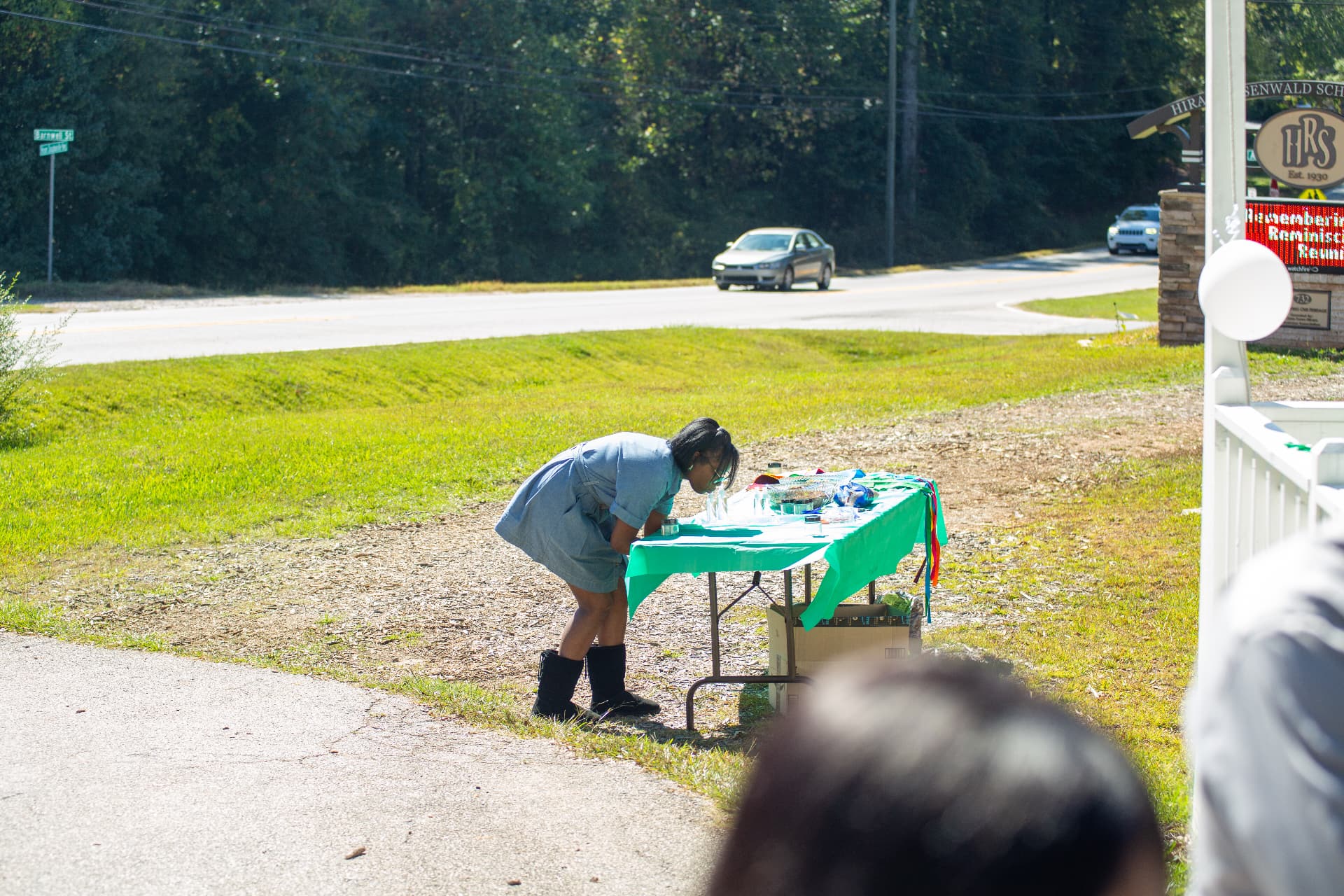 A volunteer arranges activity supplies on an outdoor table near the museum entrance sign.