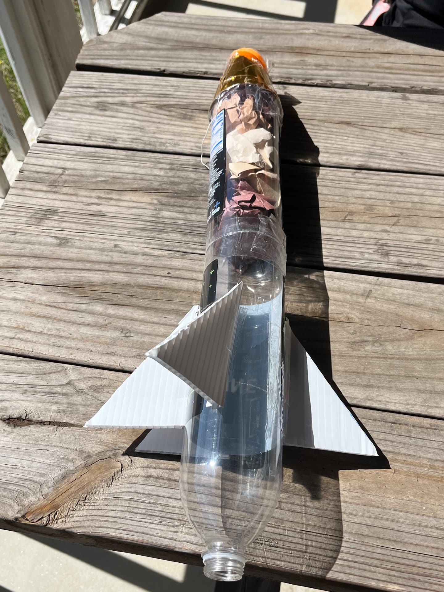 A finished bottle rocket made from a plastic water bottle with cardboard fins and a cone nose sits on a picnic table at STEM Day.