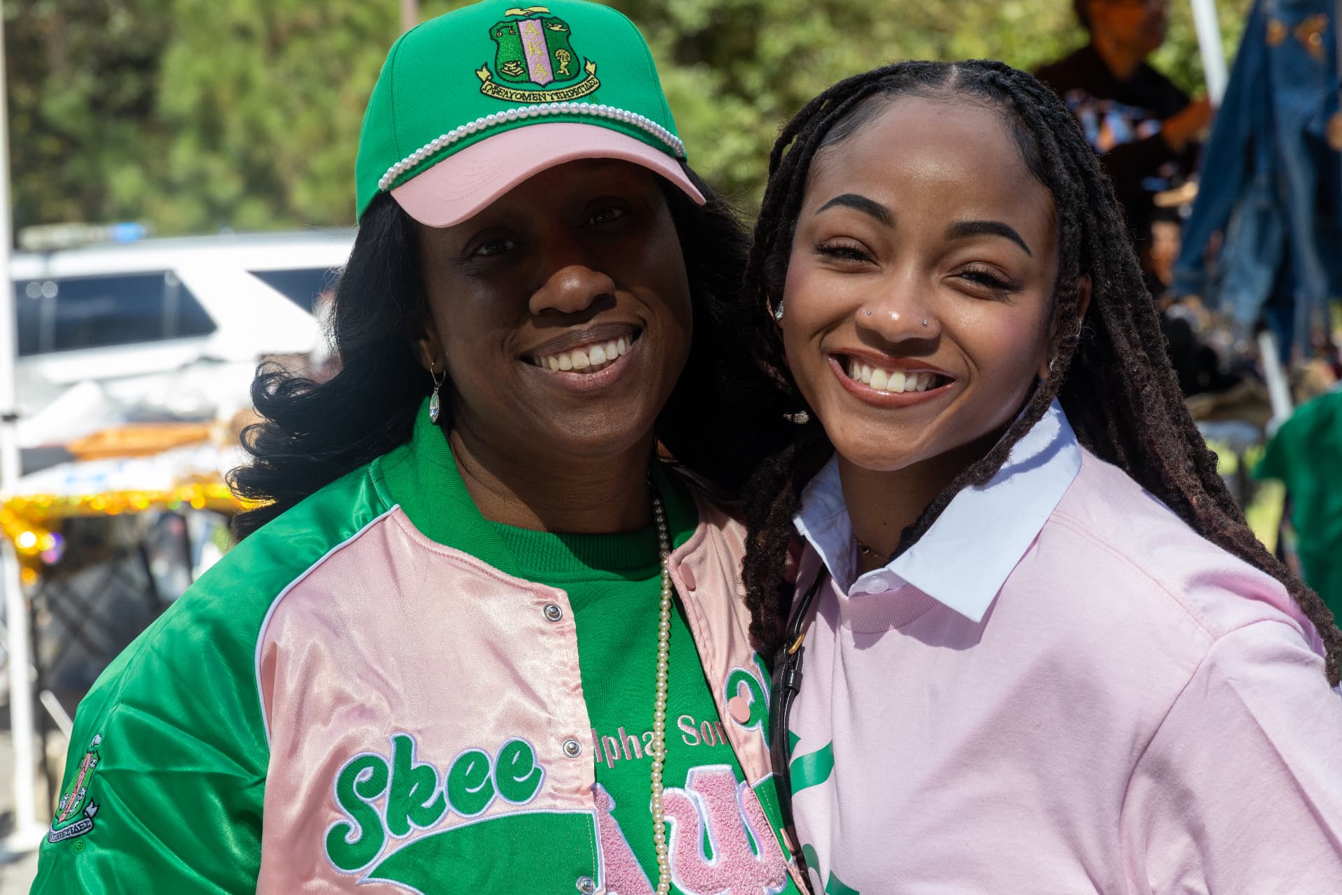 Two members of Alpha Kappa Alpha Sorority smile together in pink and green at the block party.