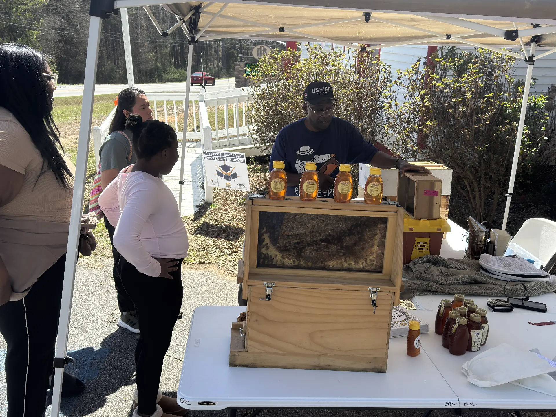 A beekeeper shows an observation hive and jars of honey to a family under a tent outside the museum.