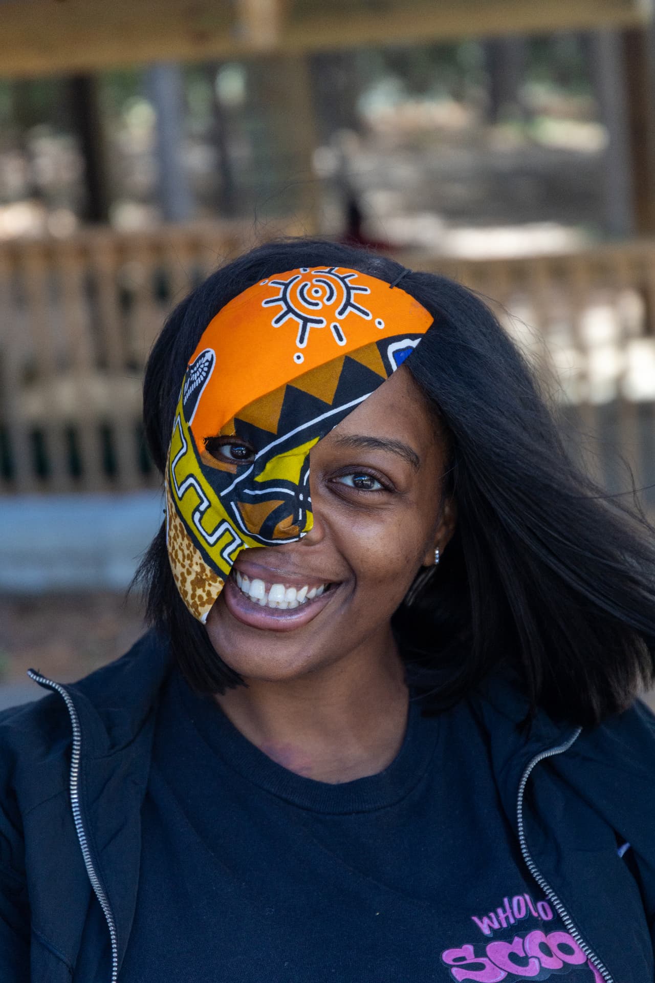 A smiling guest wears a colorful African-inspired half mask with orange, yellow and giraffe-print patterns.
