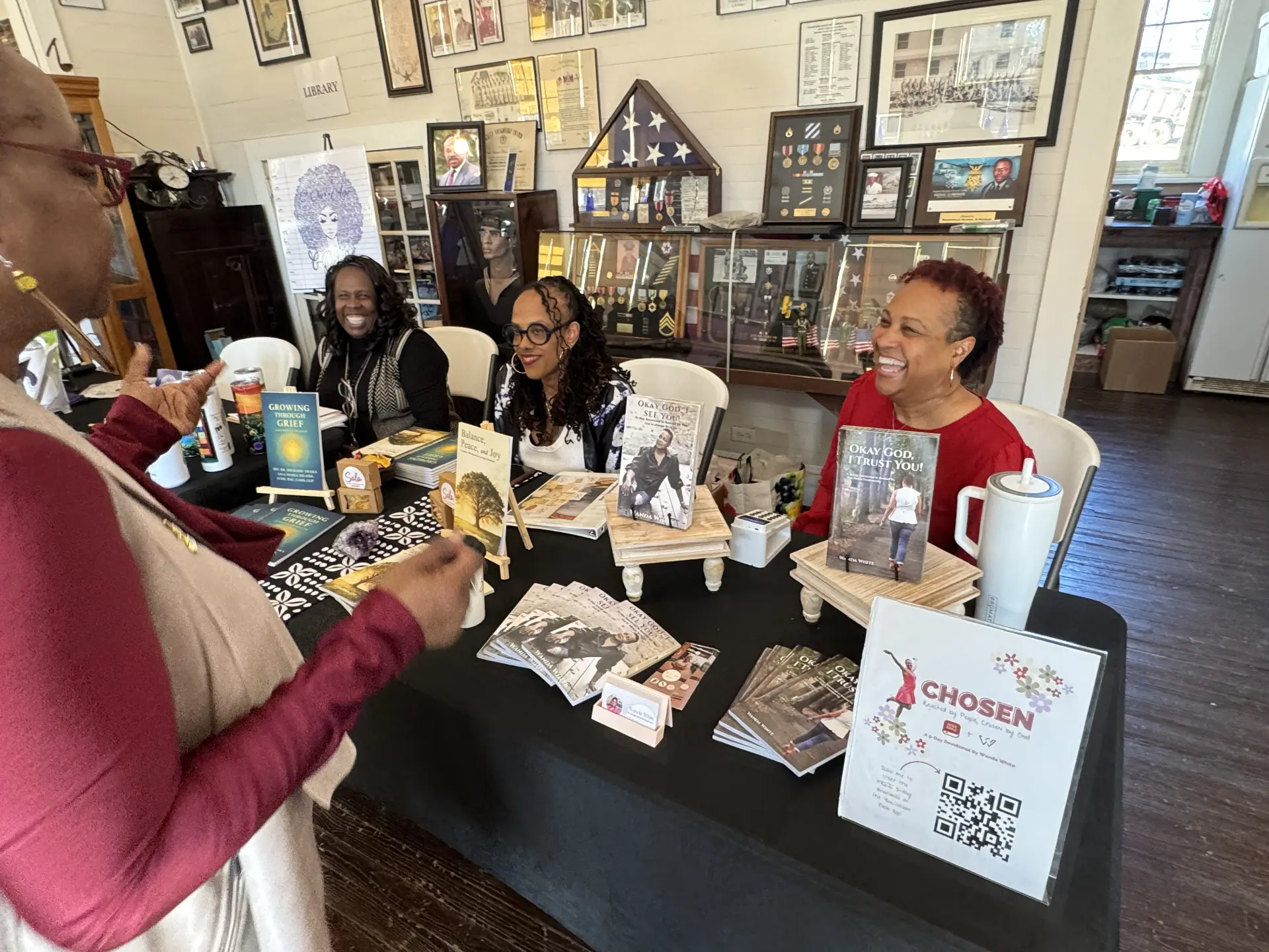 A group of women authors laugh together behind a table of inspirational books during the Authors Showcase.