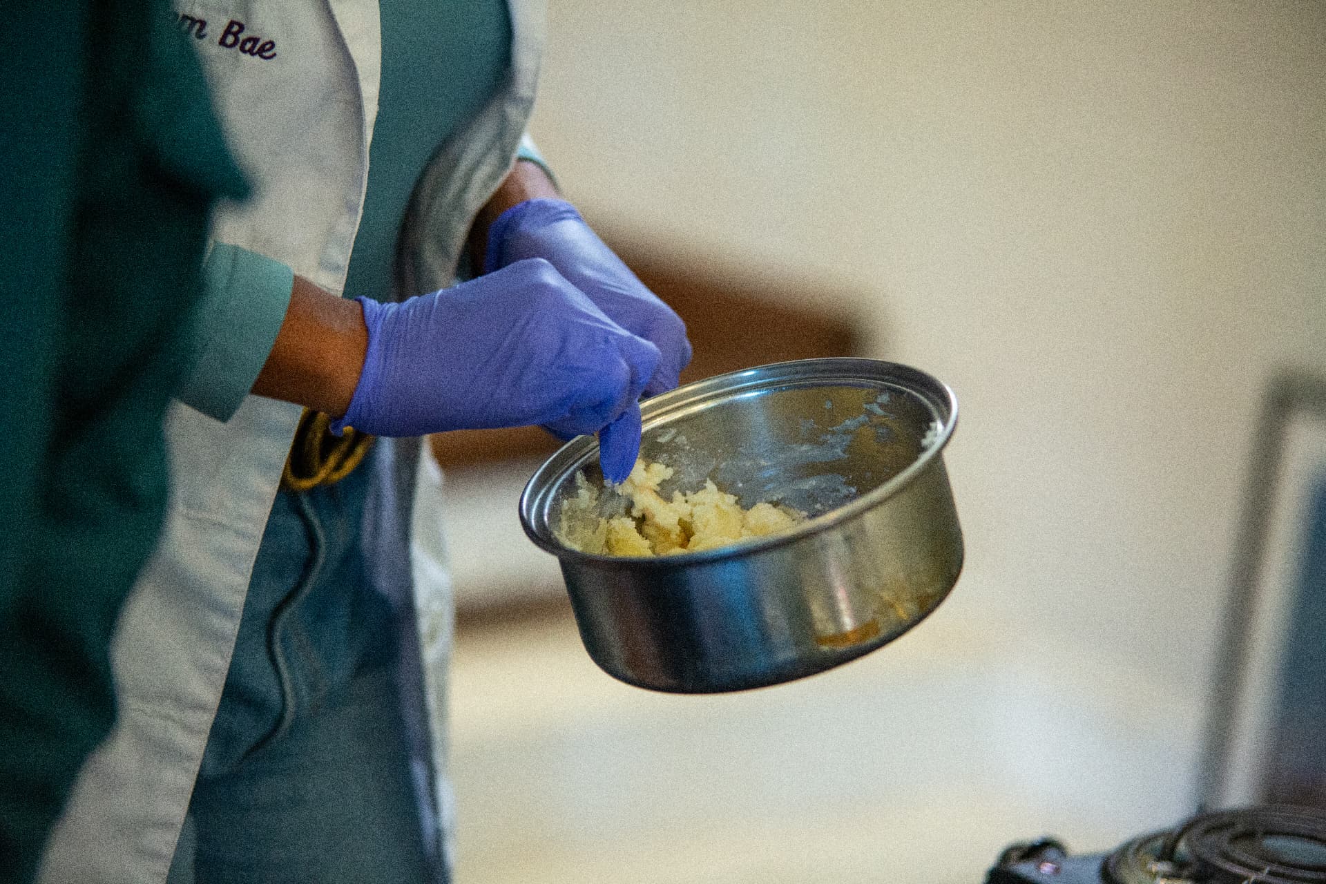 A gloved scientist mixing a yellow batch of ingredients in a saucepan during a STEM Day experiment.